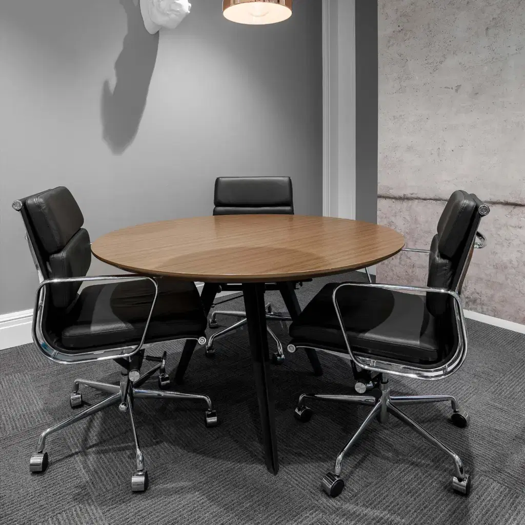 Gray dominant meeting room with a round table surrounded by black ergonomic office chairs.